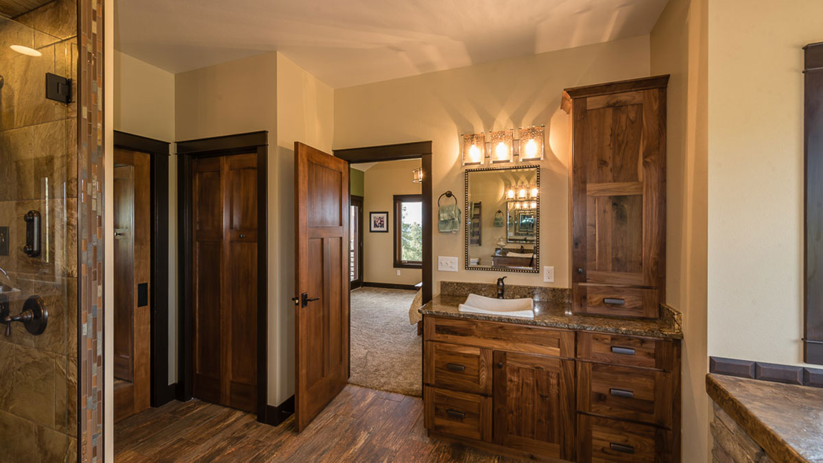 Facing the vanity with a silver mirror, granite countertop, basin sink and custom cabinets with a view into the bedroom